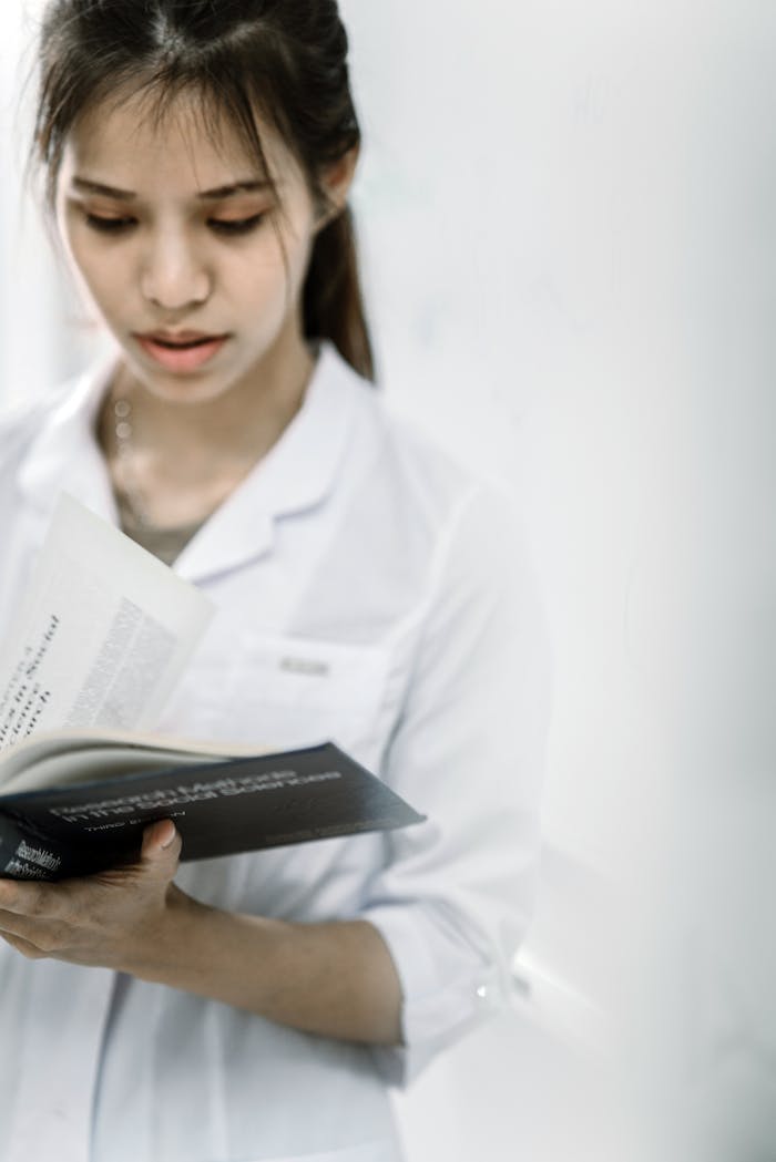 Portrait of a young woman wearing a lab coat and reading a book indoors.